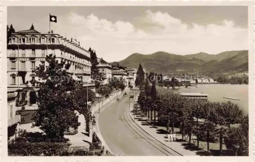 AK / Ansichtskarte LUGANO Lago di Lugano TI Quai Hotel Schweizer-Flagge Tramgleis Luganersee Promenade Berge Baeume