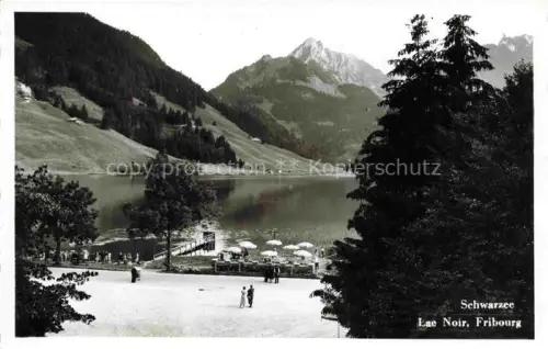 AK / Ansichtskarte Schwarzsee Lac Noir 1050m Sense FR Lac-Noir See Berge Tannenwald Sonnenschirme Badestrand Spaziergaenger Steg