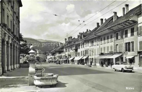 AK / Ansichtskarte Nidau Niedau Bielersee Lac de Bienne BE Hauptstrasse Brunnen Geschaefte Strassenbahnkabel Autos Altstadt