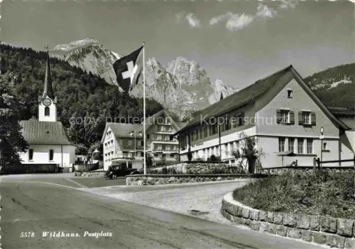 AK / Ansichtskarte Wildhaus  Toggenburg SG Postplatz Kirche Schweizer-Fahne Dorfplatz Berge Churfirsten Auto