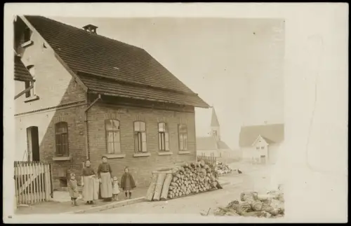 Backsteinhaus mit Familie  Holzstapel, Kirche im Hintergrund 1910 Privatfoto